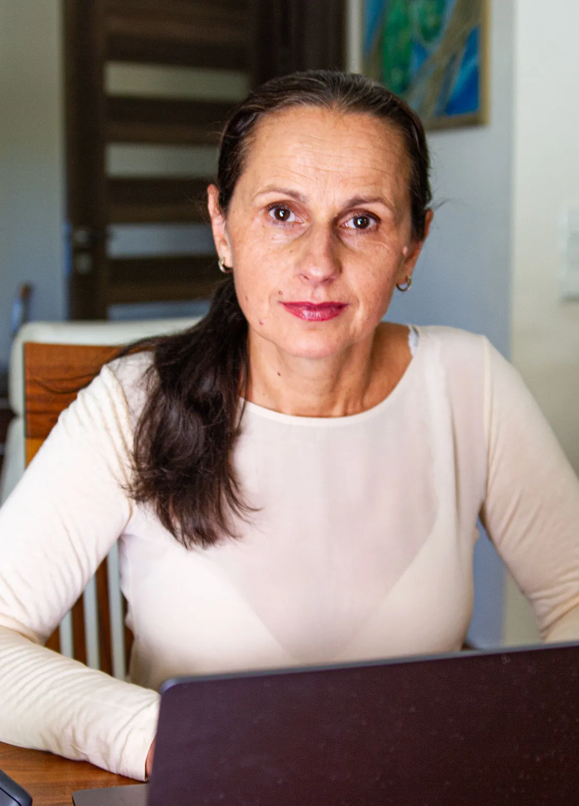 Anna Stec sitzt an ihrem Holztisch hinter dem Laptop und blickt ruhig in die Kamera